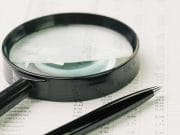 Photo of a magnifying glass and a pen.